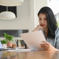 Serious young businesswoman reading statistics document, planning business strategy at office desk