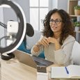 Smiling middle-aged woman recording podcast in a home studio with a laptop, microphone, and ring light