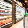 woman hand hold supermarket shopping cart with abstract blur organic fresh fruits and vegetable on shelves in grocery store defocused bokeh light background